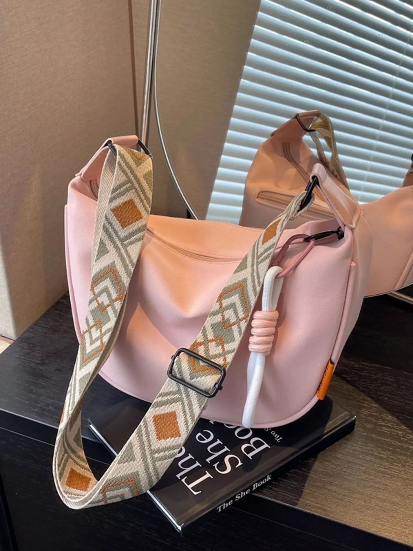 Blush canvas crossbody bag with adjustable geometric strap displayed on a tabletop for everyday styling