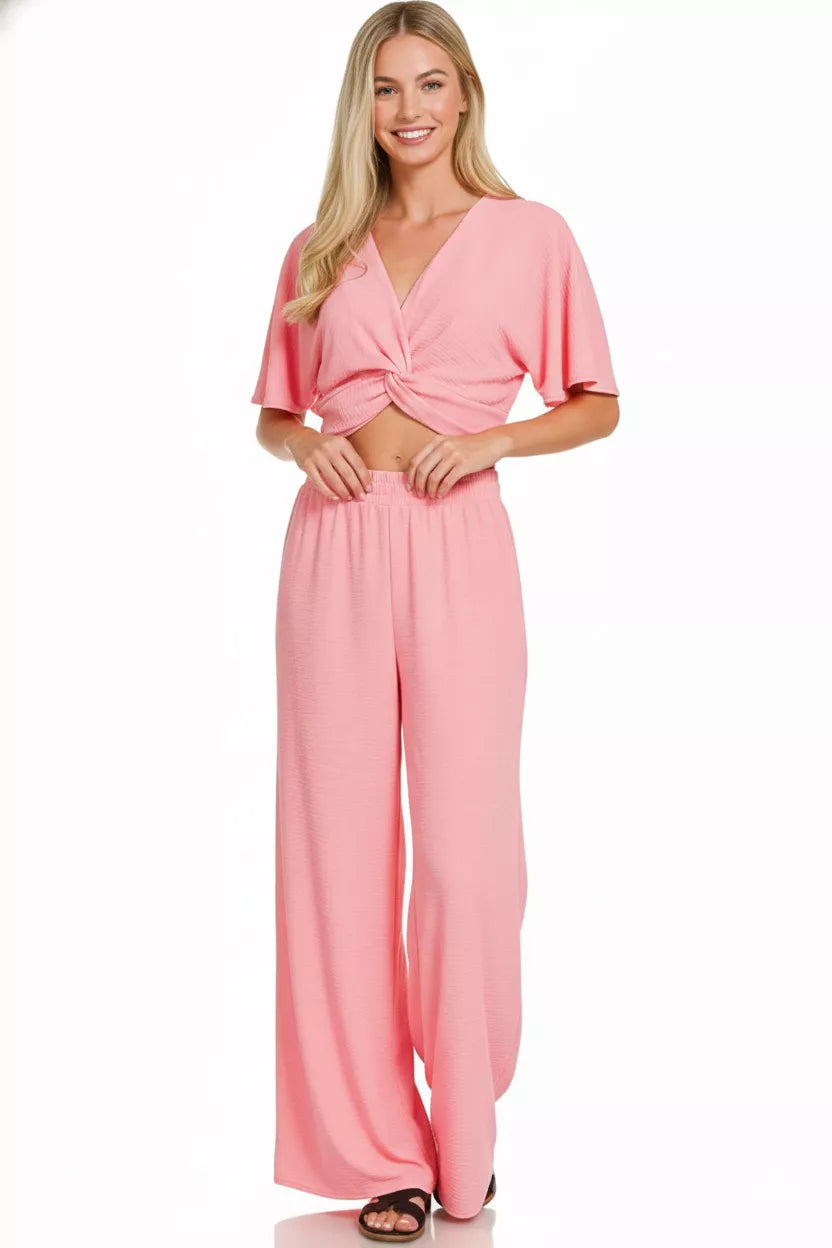 Blush pink twisted crop top and wide leg pants two-piece woven set with flutter sleeves and flowy silhouette.