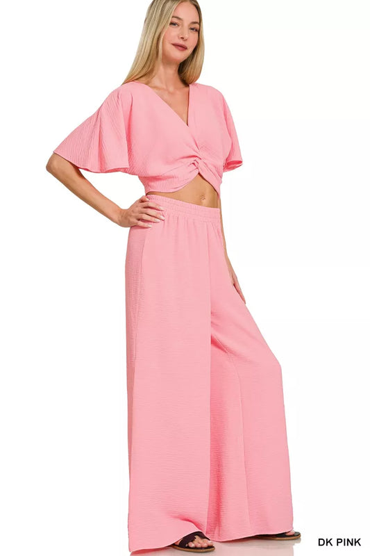 Blush pink twisted crop top and wide leg pants two-piece woven set with flutter sleeves and flowy silhouette.
