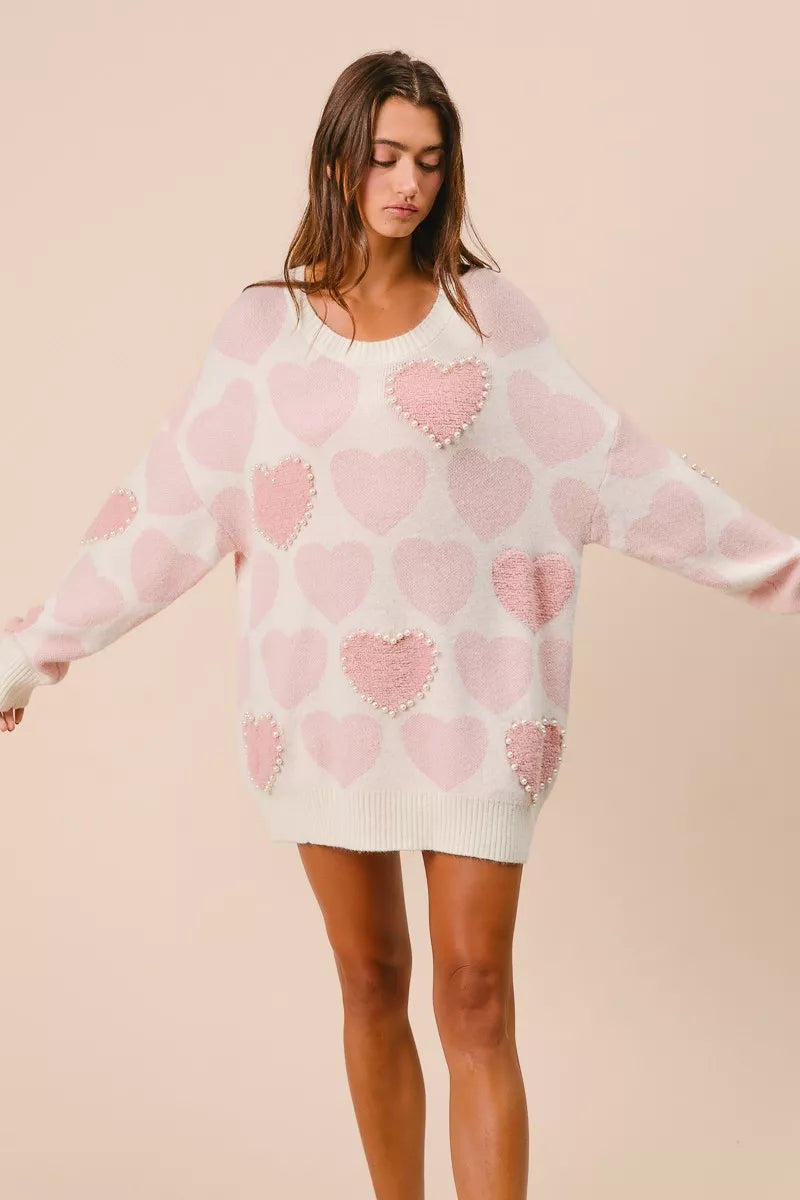 Woman wearing a cream knit sweater with pink heart pattern and pearl embellishments