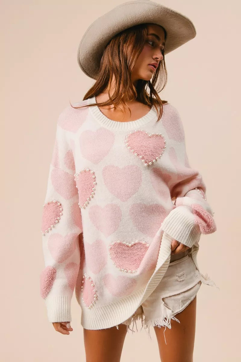 Woman wearing a cream knit sweater with pink heart pattern and pearl embellishments