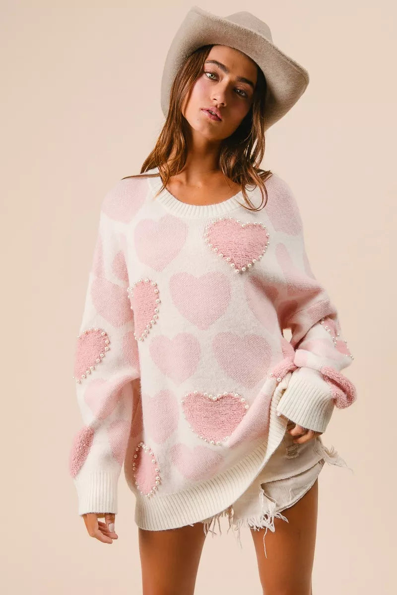 Woman wearing a cream knit sweater with pink heart pattern and pearl embellishments