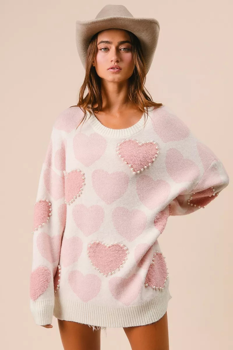 Woman wearing a cream knit sweater with pink heart pattern and pearl embellishments