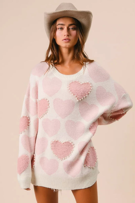Woman wearing a cream knit sweater with pink heart pattern and pearl embellishments