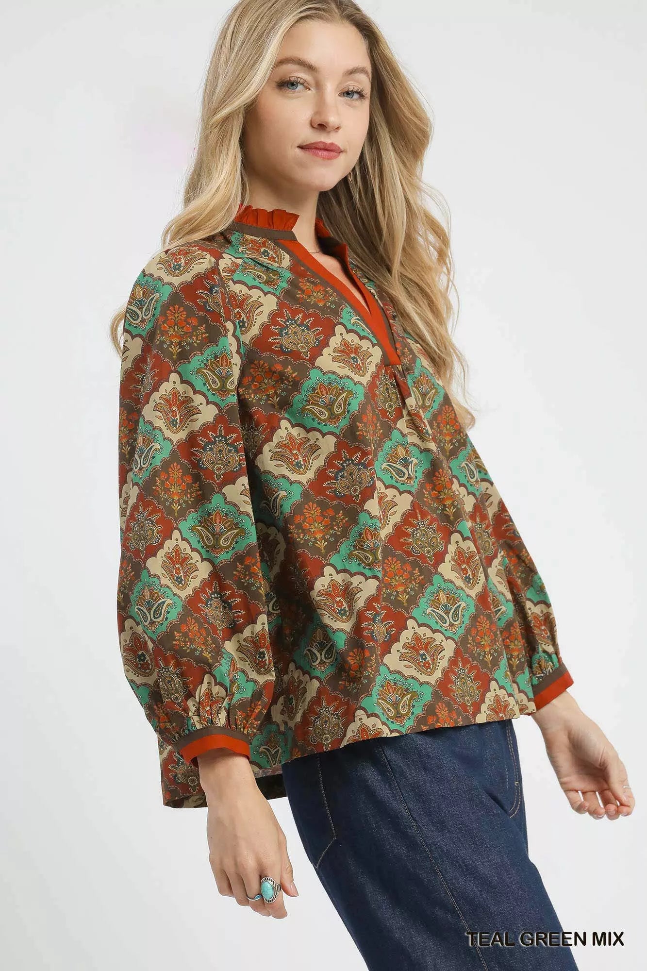 Woman wearing an abstract print ruffle neck top with earthy tones and long sleeves.