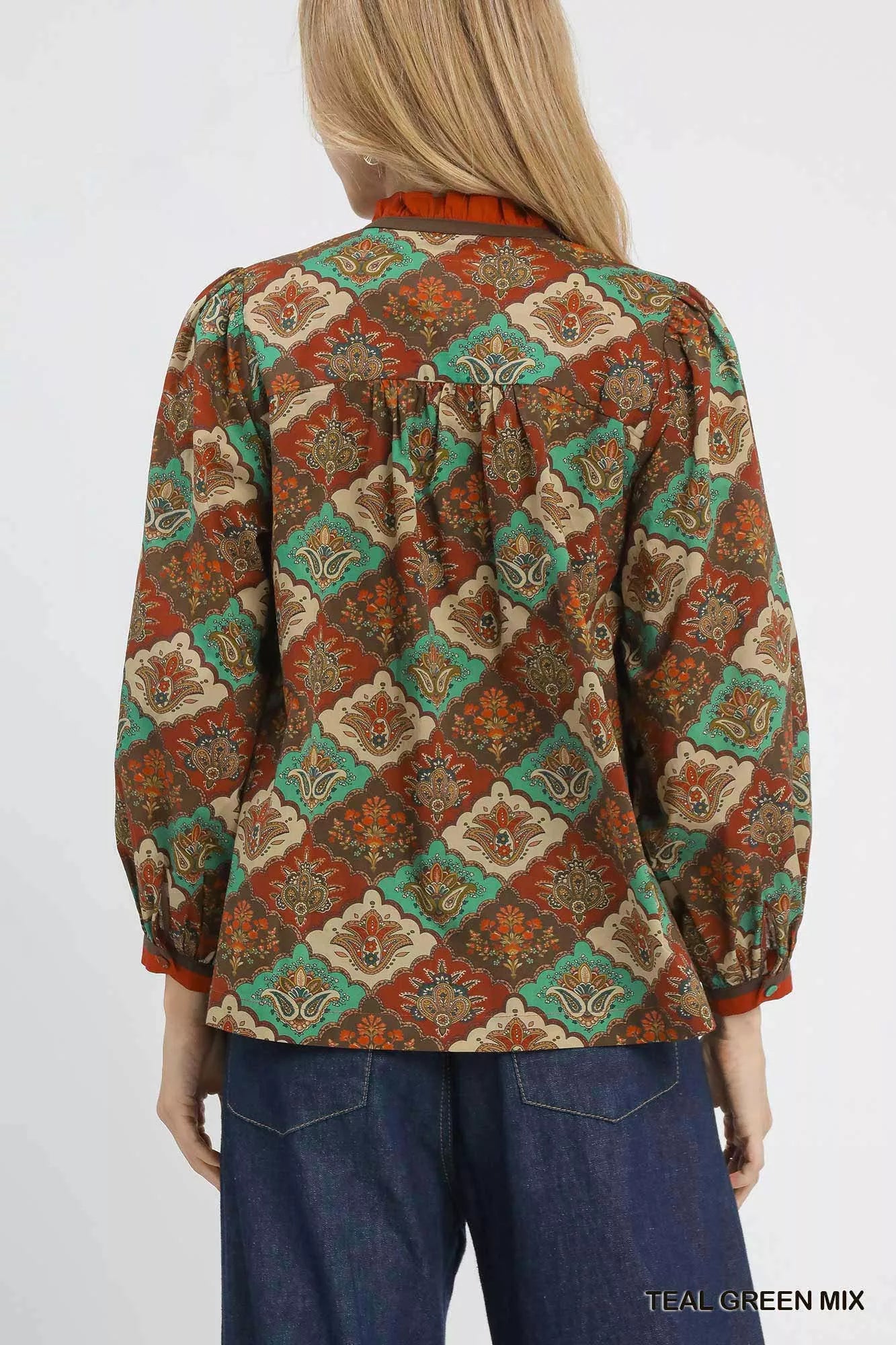 Woman wearing an abstract print ruffle neck top with earthy tones and long sleeves.
