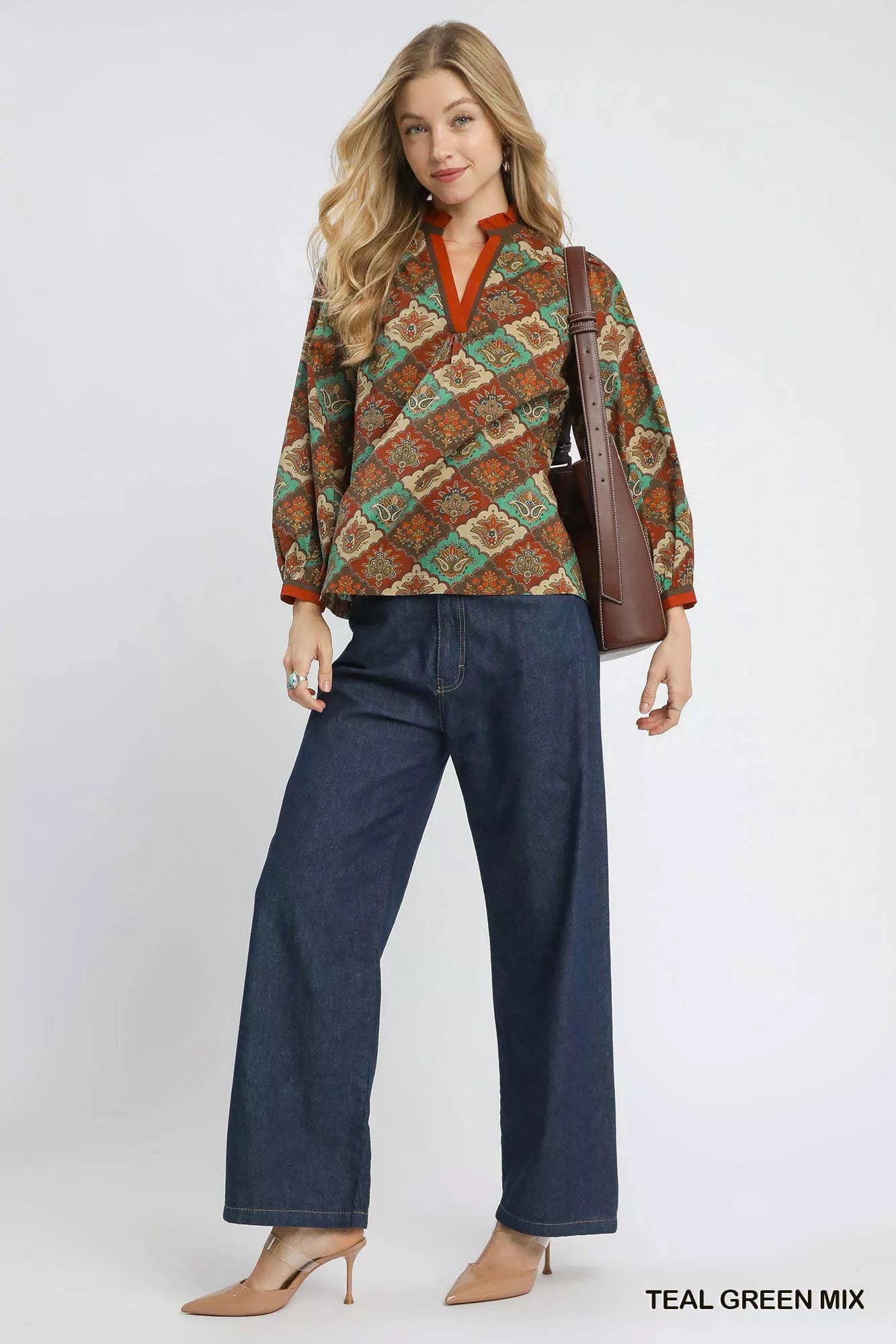 Woman wearing an abstract print ruffle neck top with earthy tones and long sleeves.