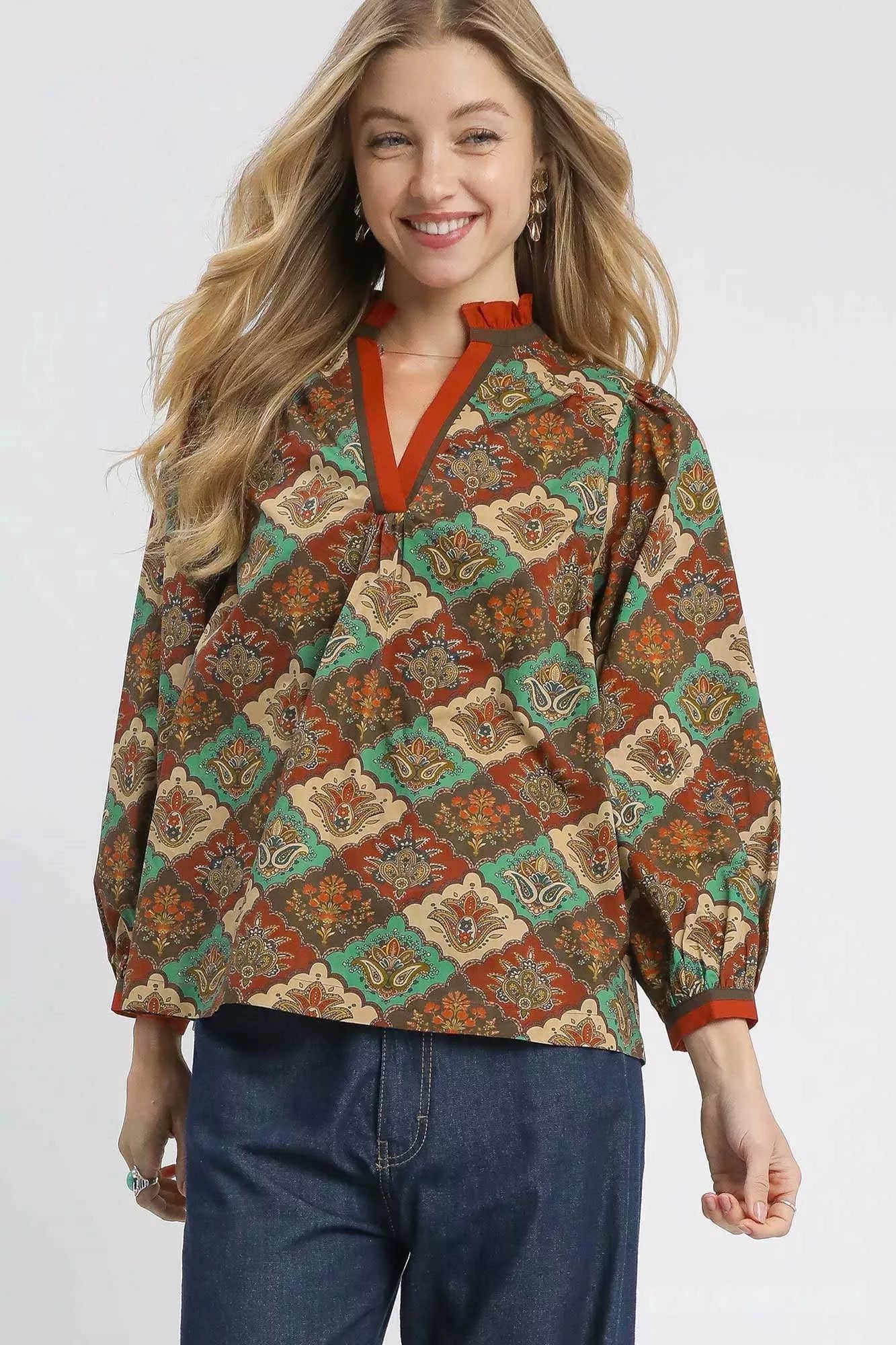 Woman wearing an abstract print ruffle neck top with earthy tones and long sleeves.