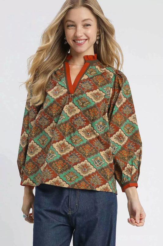 Woman wearing an abstract print ruffle neck top with earthy tones and long sleeves.