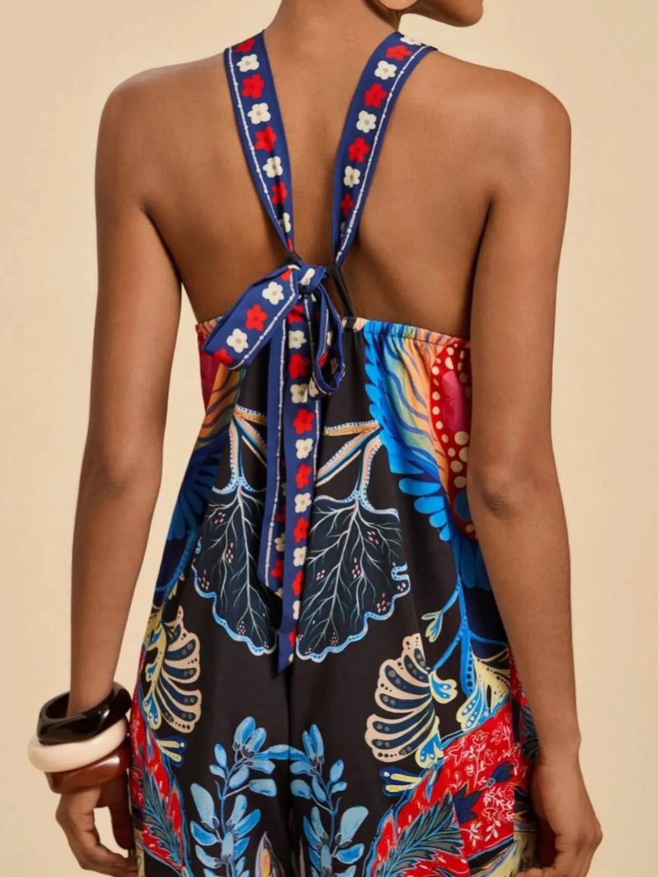 Model wearing royal blue and black Boho Breeze Halter Jumpsuit with vibrant floral and bird patterns, halter neckline, and wide-leg silhouette.