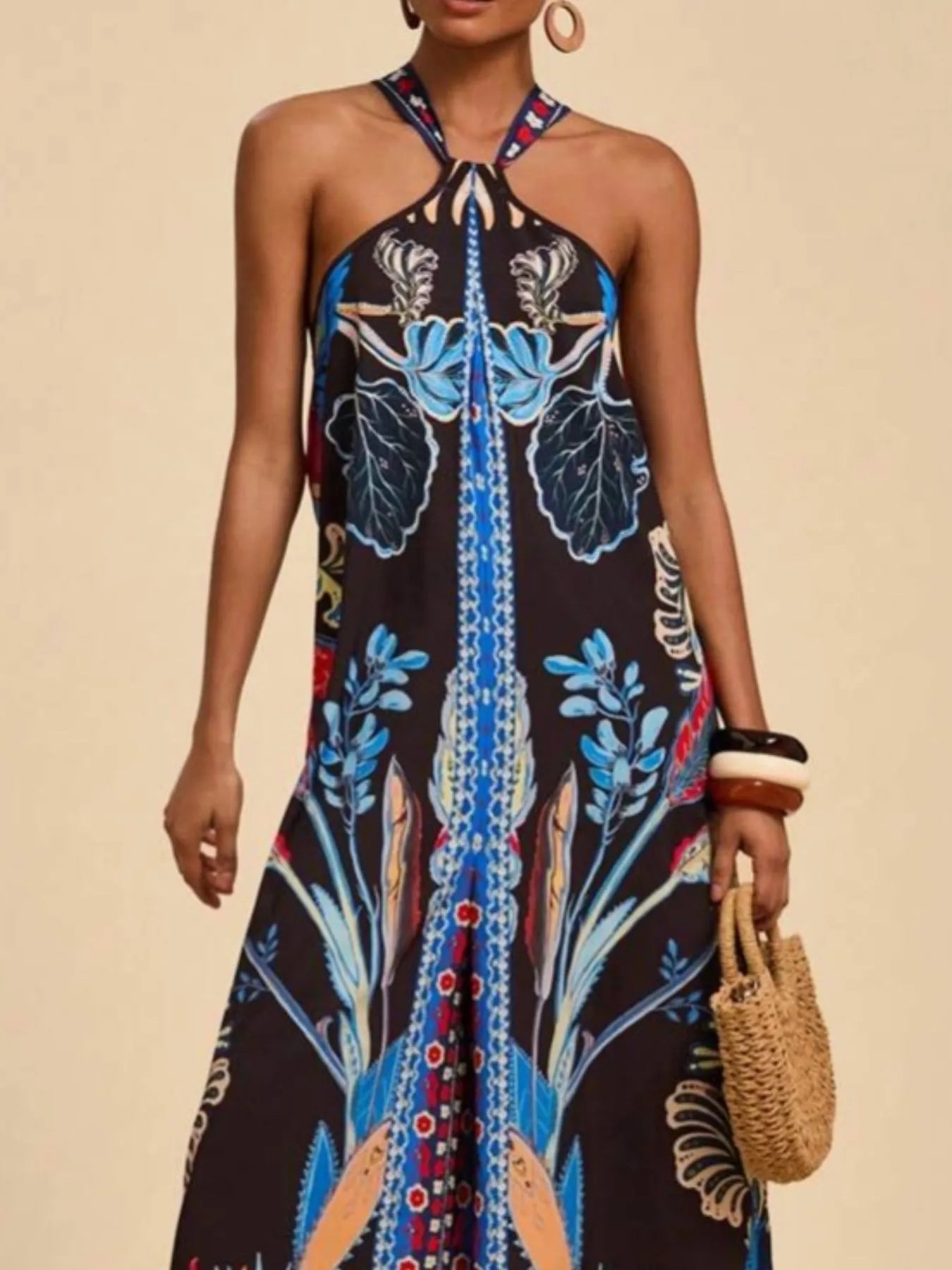 Model wearing royal blue and black Boho Breeze Halter Jumpsuit with vibrant floral and bird patterns, halter neckline, and wide-leg silhouette.
