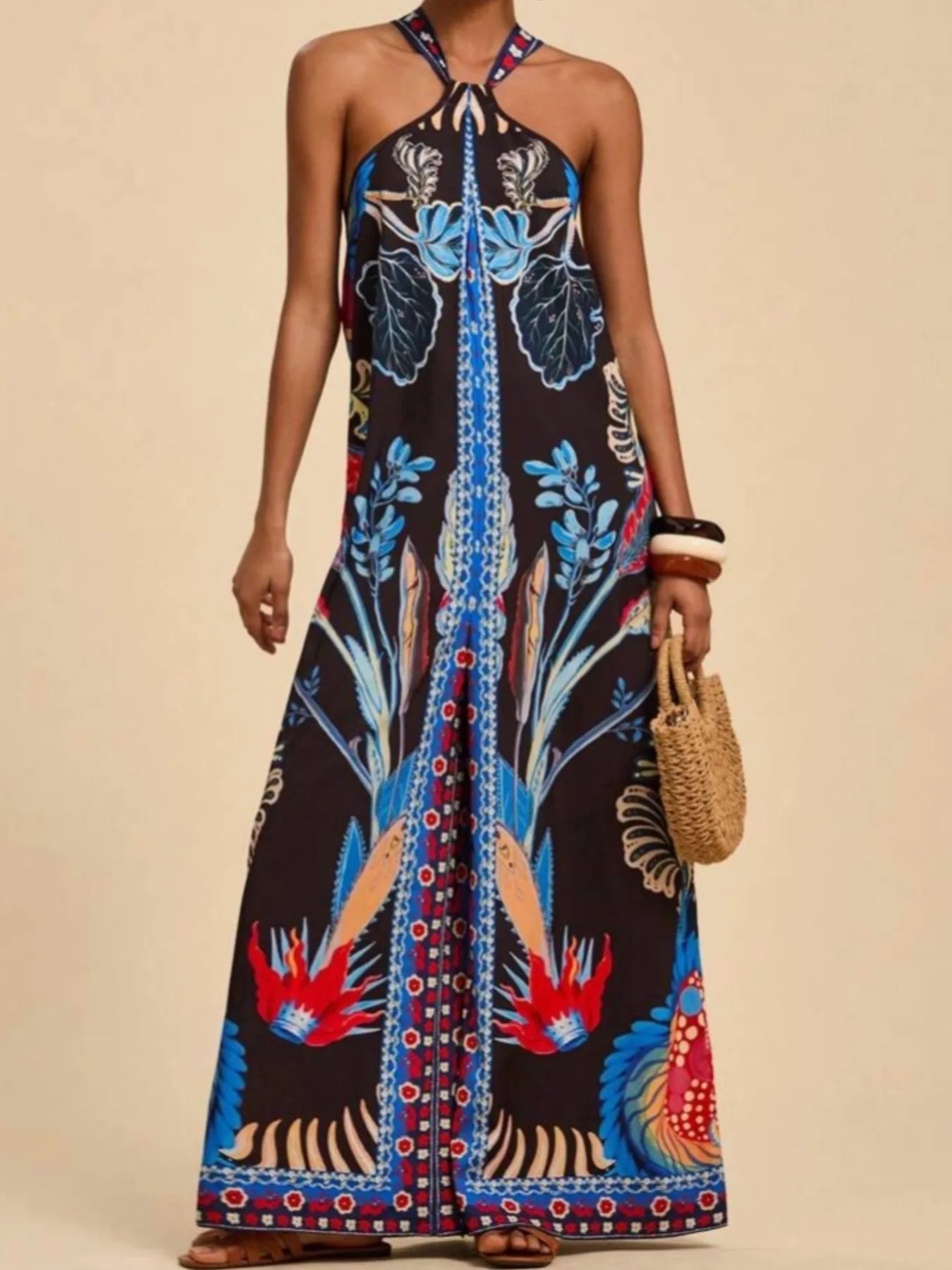 Model wearing royal blue and black Boho Breeze Halter Jumpsuit with vibrant floral and bird patterns, halter neckline, and wide-leg silhouette.