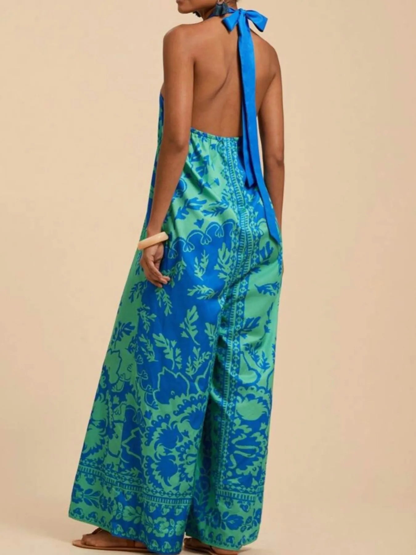 Model wearing sky blue Boho Breeze Halter Jumpsuit with leafy patterns, halter neckline, and wide-leg flowy fit.