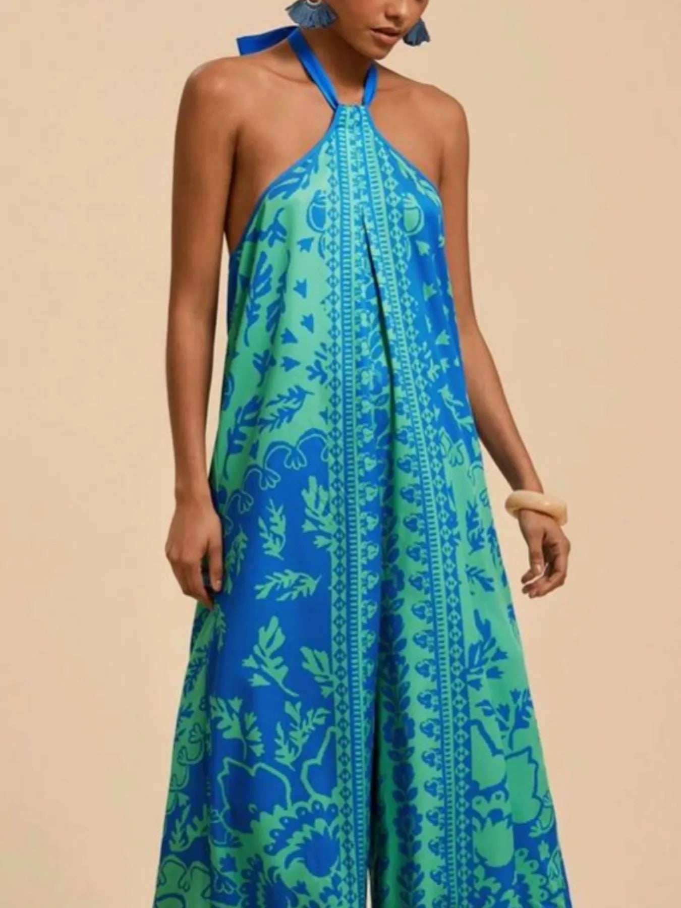 Model wearing sky blue Boho Breeze Halter Jumpsuit with leafy patterns, halter neckline, and wide-leg flowy fit.