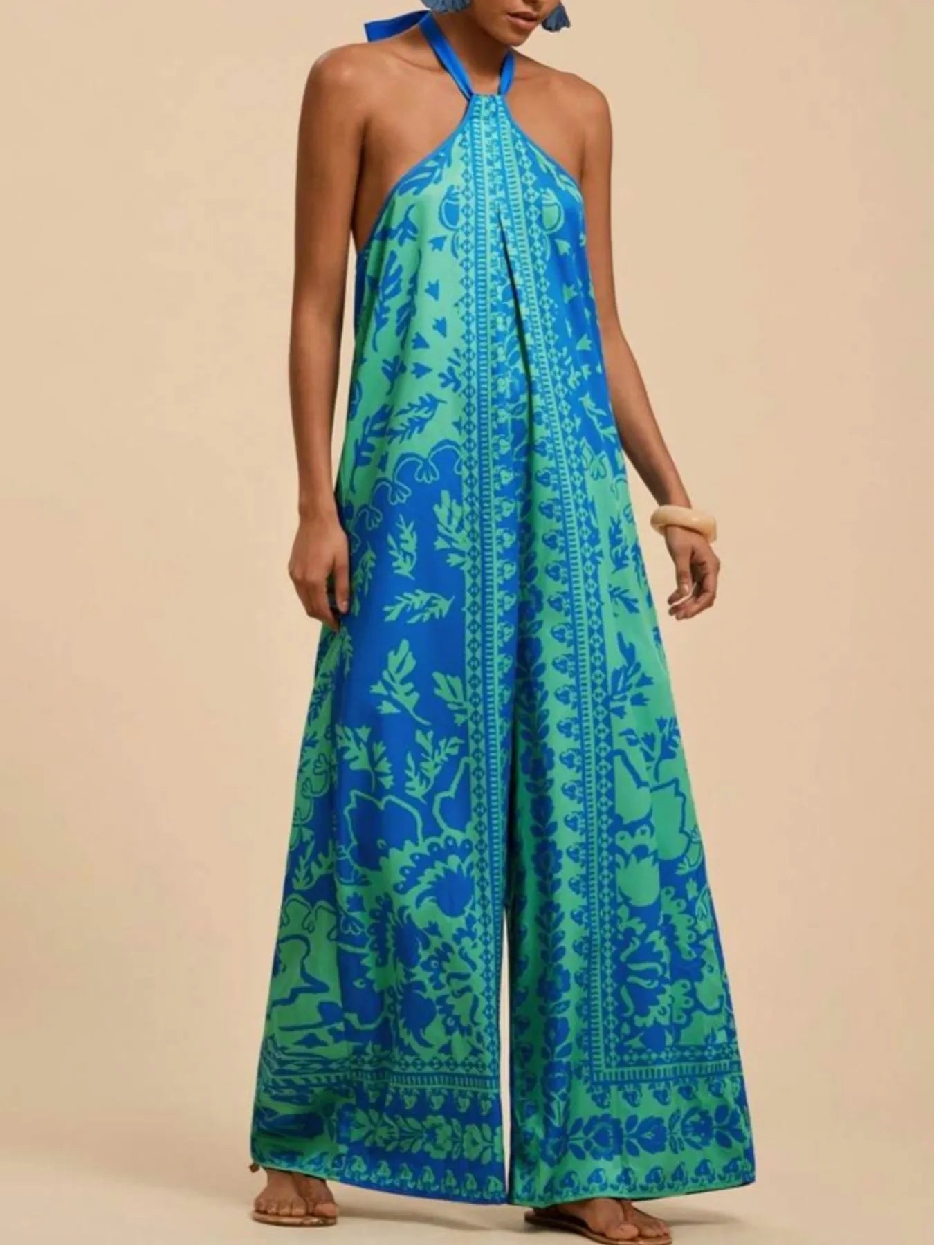 Model wearing sky blue Boho Breeze Halter Jumpsuit with leafy patterns, halter neckline, and wide-leg flowy fit.