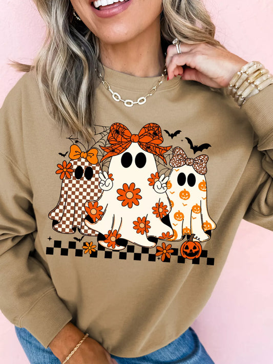 Woman wearing a tan crewneck sweatshirt with three cute boho-style ghosts featuring bows and floral pumpkin patterns — Halloween sweatshirt from A Whimsical Affair.