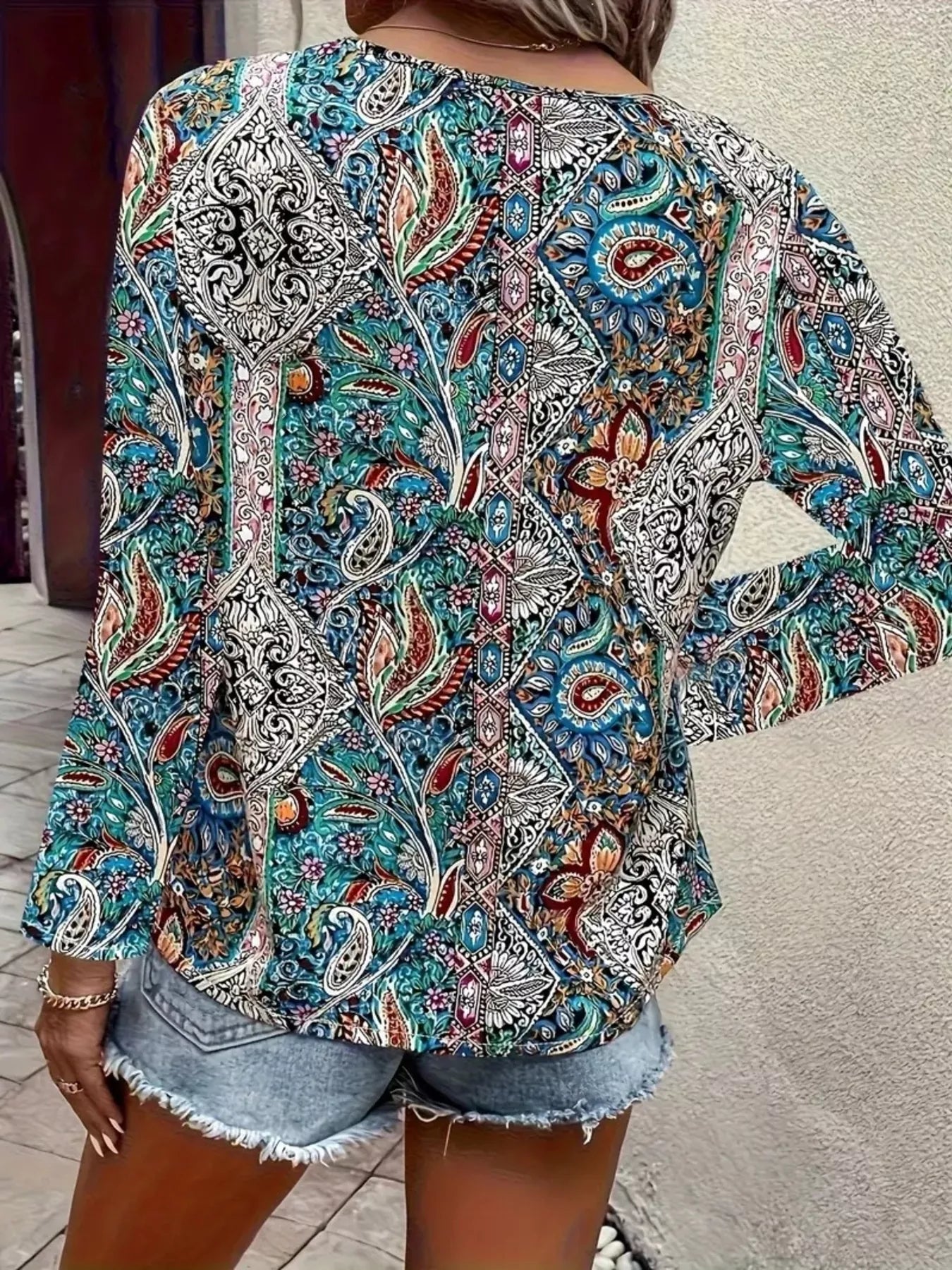 Boho paisley patchwork blouse with a V-neckline, flowy long sleeves, and relaxed slightly stretchy fit styled with denim shorts.
