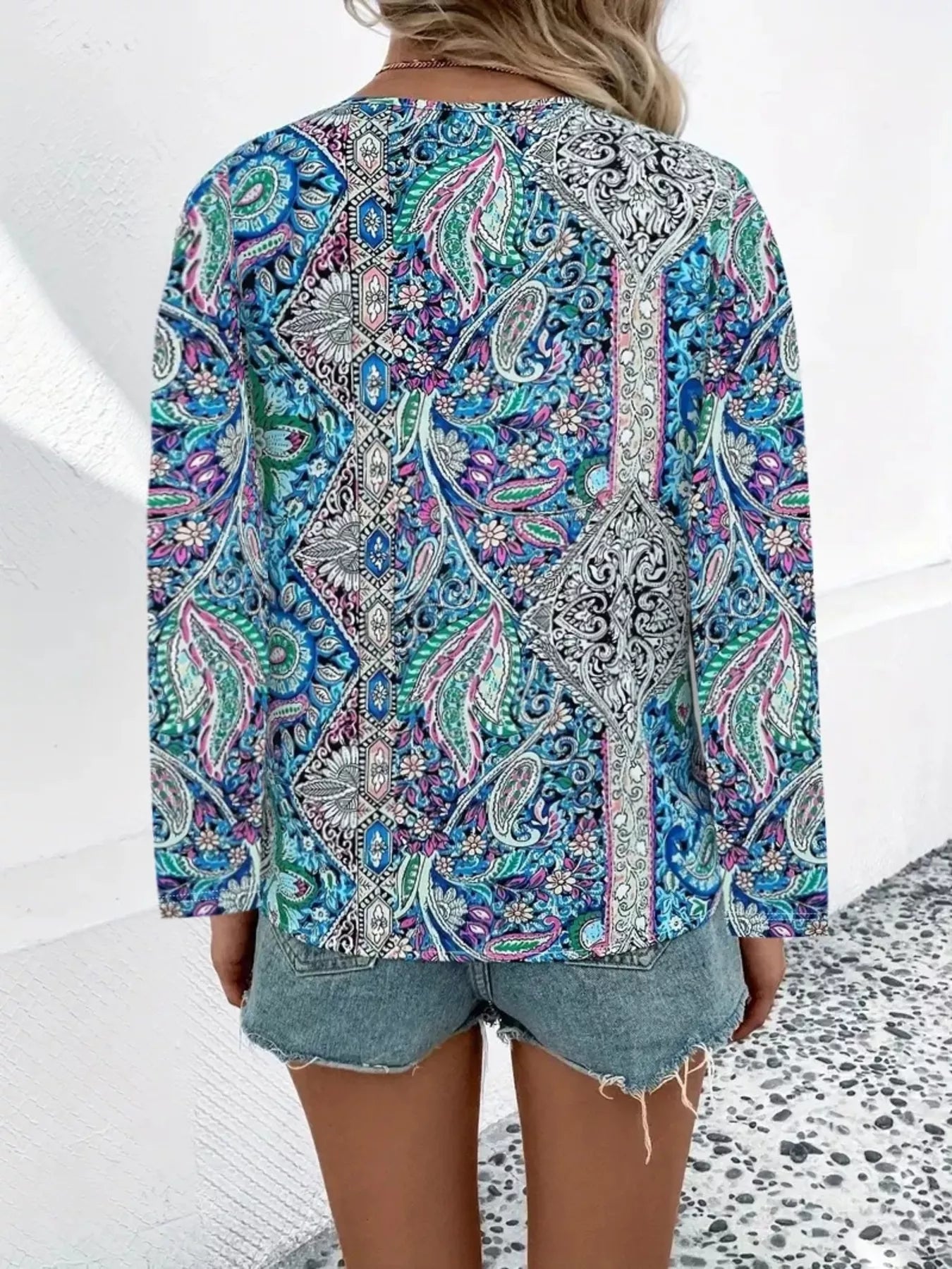 Boho paisley patchwork blouse with a V-neckline, flowy long sleeves, and relaxed slightly stretchy fit styled with denim shorts.