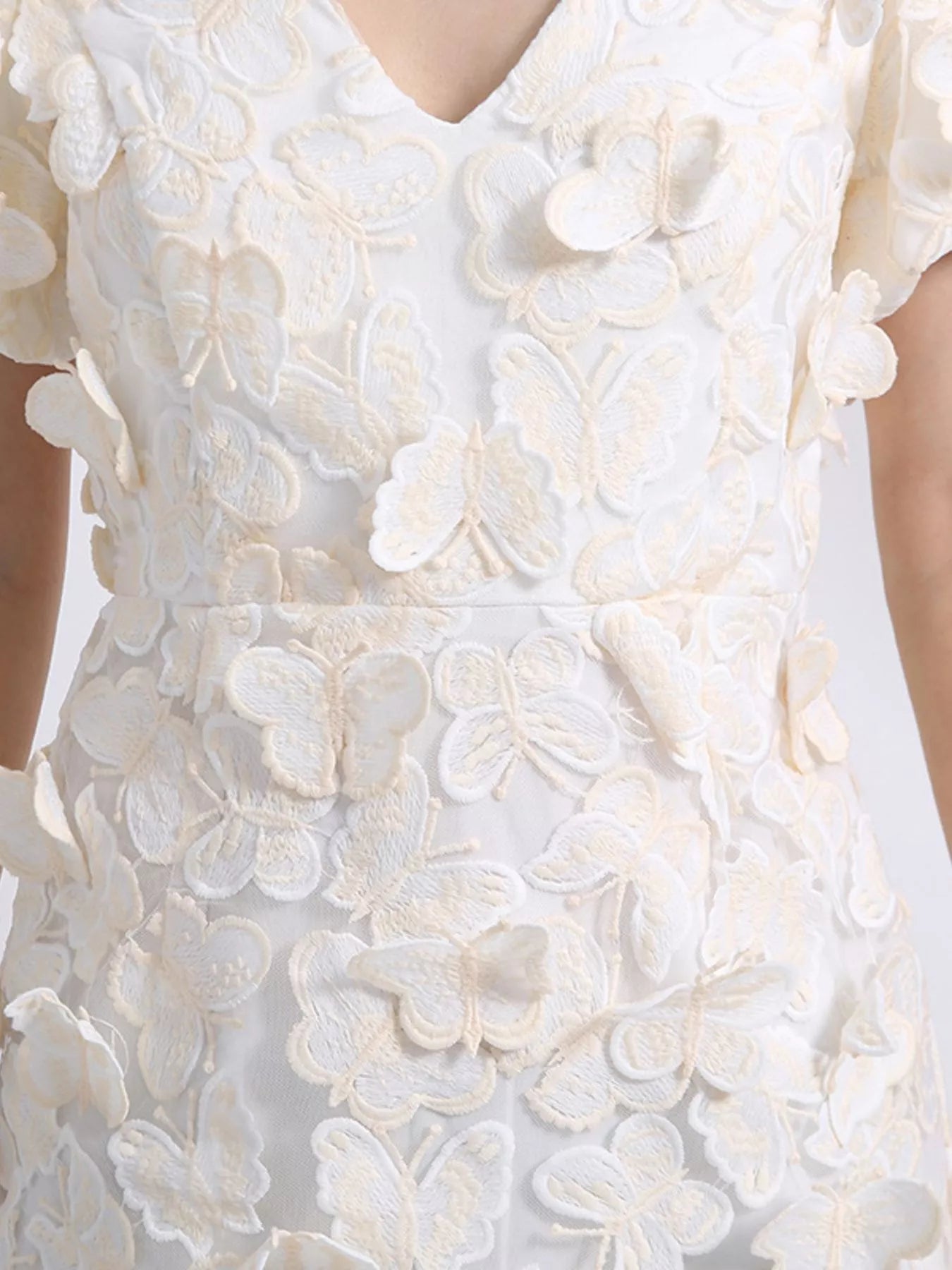 Model wearing a white mini dress adorned with 3D butterfly appliqués, featuring short puff sleeves, a V-neckline, and a fitted silhouette, styled against a plain background.