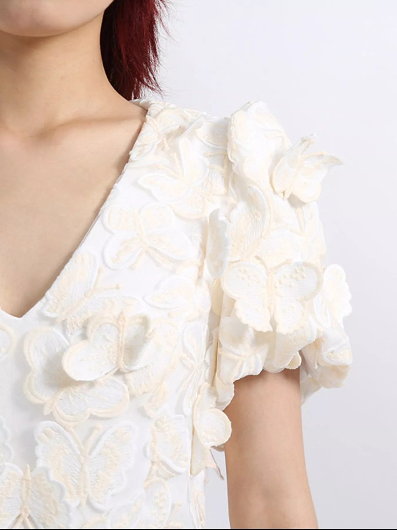 Model wearing a white mini dress adorned with 3D butterfly appliqués, featuring short puff sleeves, a V-neckline, and a fitted silhouette, styled against a plain background.