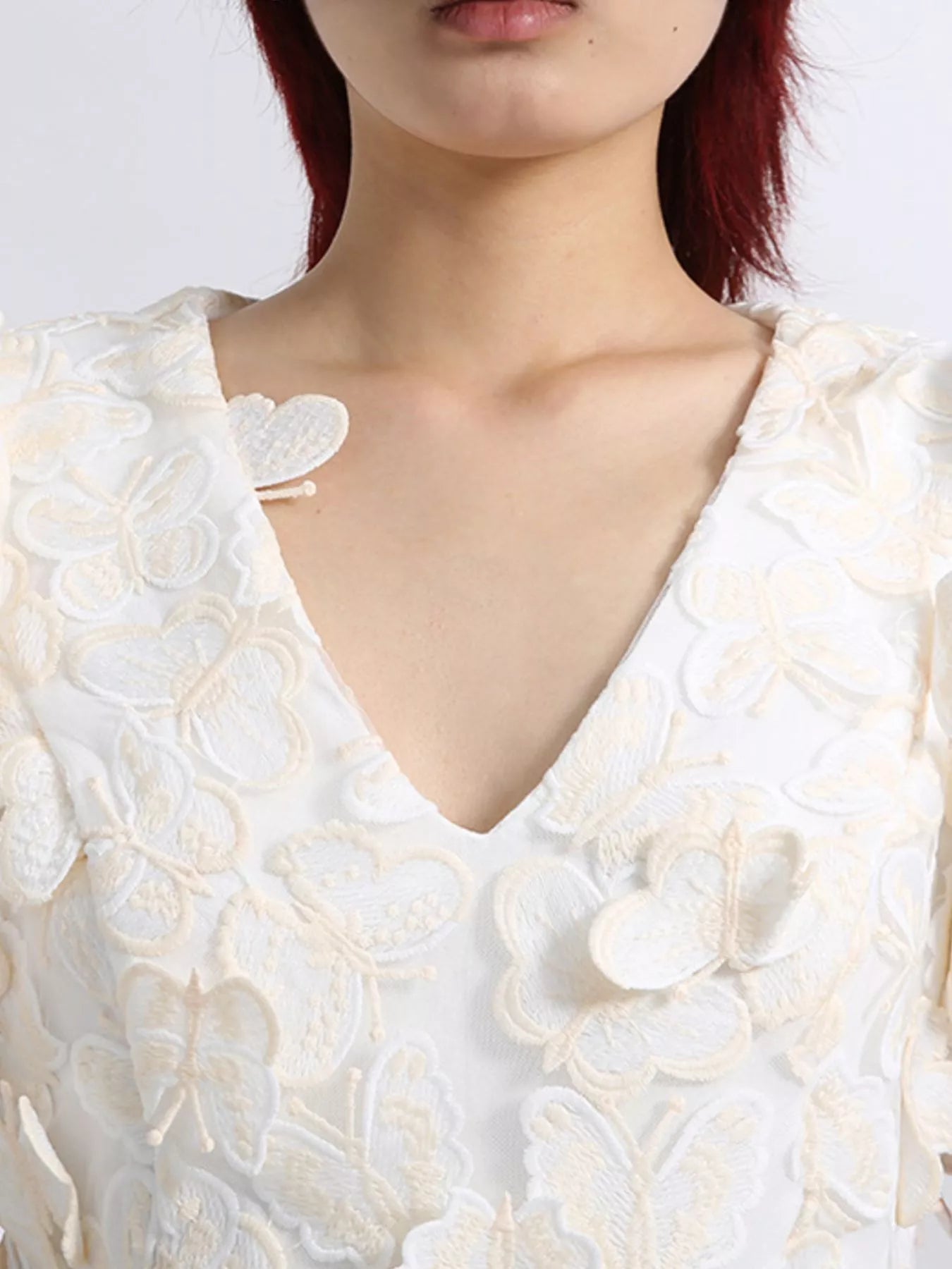 Model wearing a white mini dress adorned with 3D butterfly appliqués, featuring short puff sleeves, a V-neckline, and a fitted silhouette, styled against a plain background.