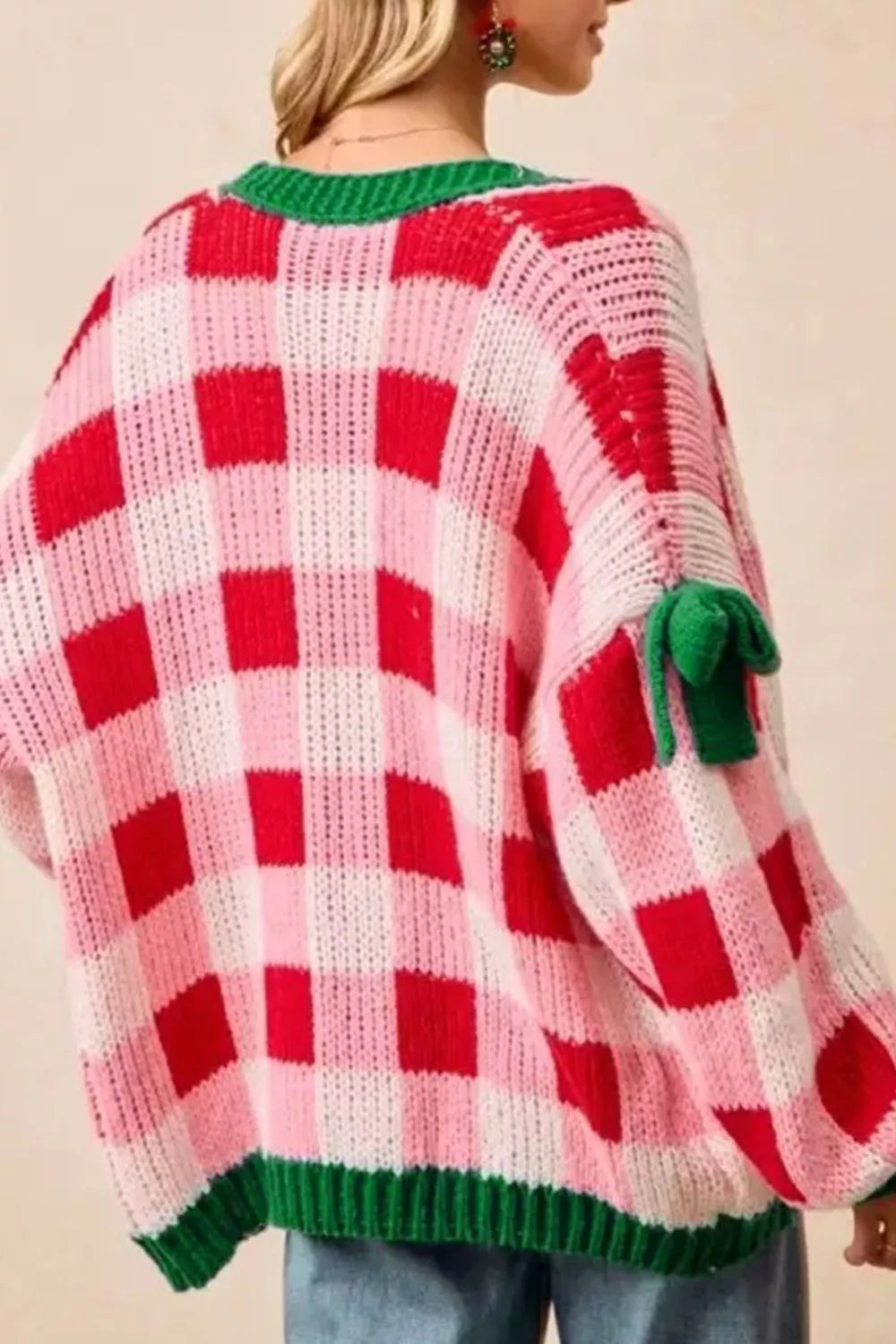 Festive pink and red checker knit cardigan with green trim and bow details on sleeves.