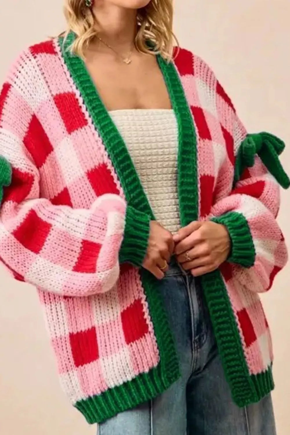 Festive pink and red checker knit cardigan with green trim and bow details on sleeves.