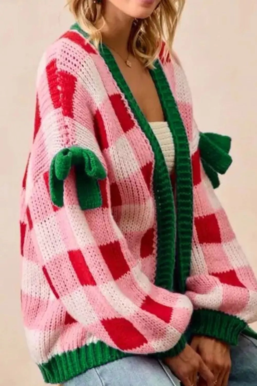 Festive pink and red checker knit cardigan with green trim and bow details on sleeves.