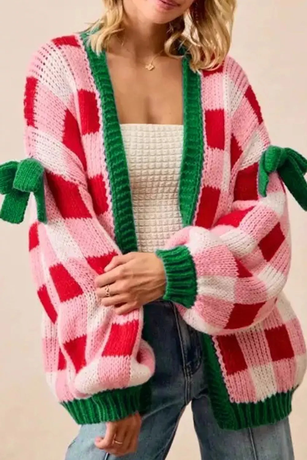Festive pink and red checker knit cardigan with green trim and bow details on sleeves.
