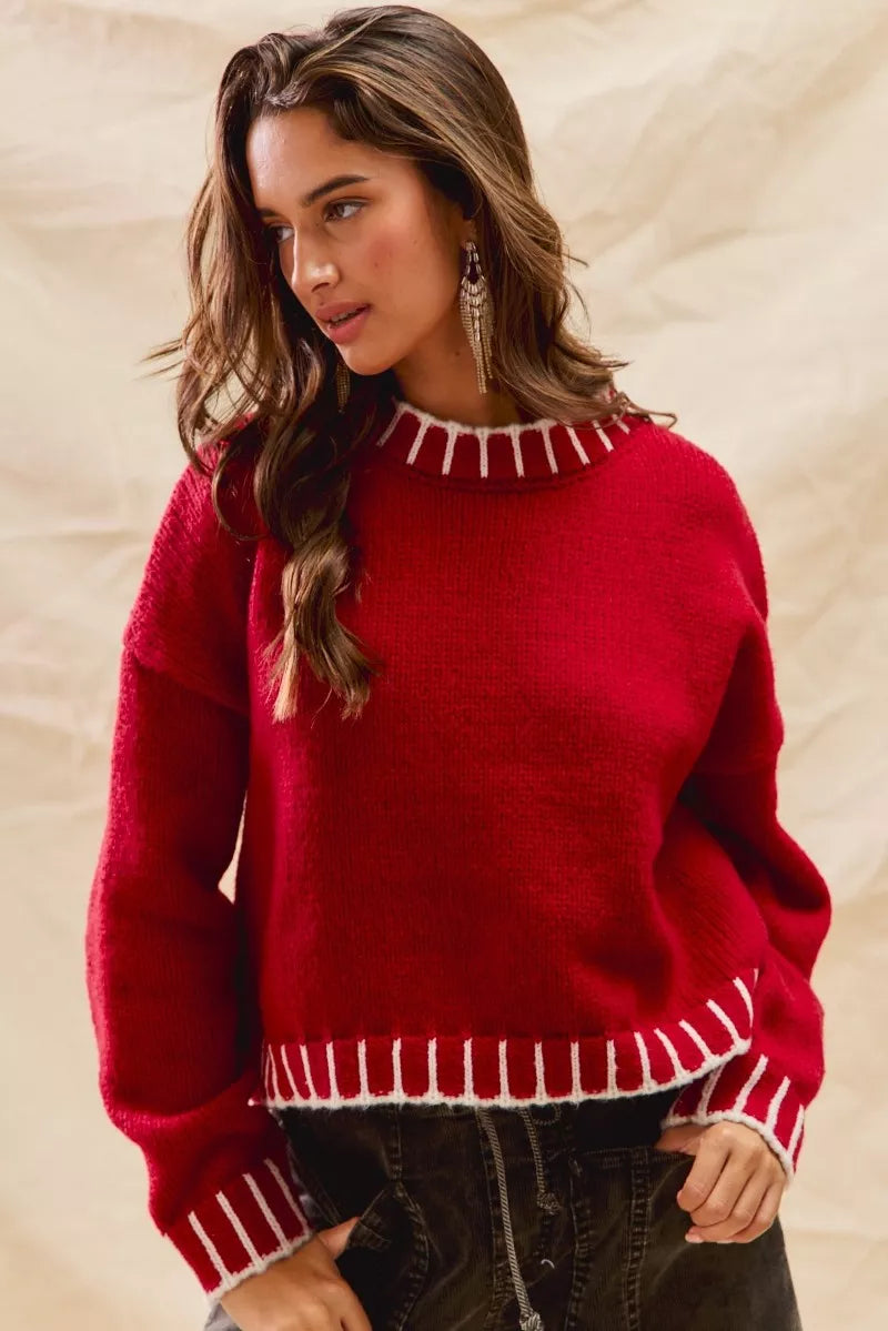 Woman wearing a red sweater with white contrast stitching along the collar, cuffs, and hem — cozy holiday sweater from A Whimsical Affair.