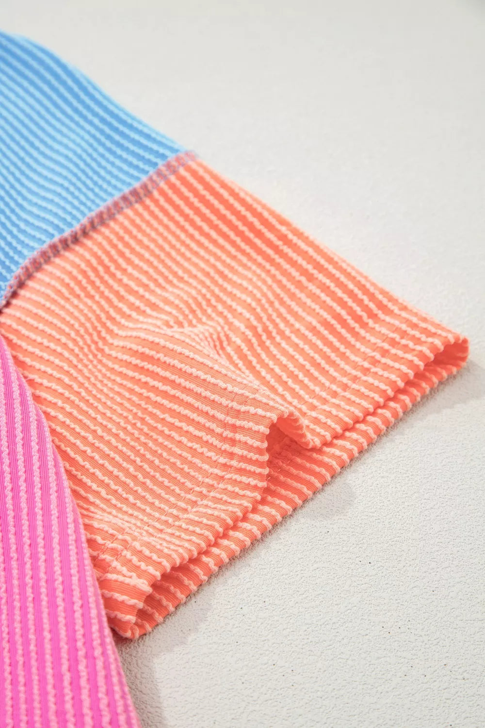 Color block ribbed V-neck tee with pink body, blue shoulders, orange sleeves, seam details, and slightly stretchy fit.