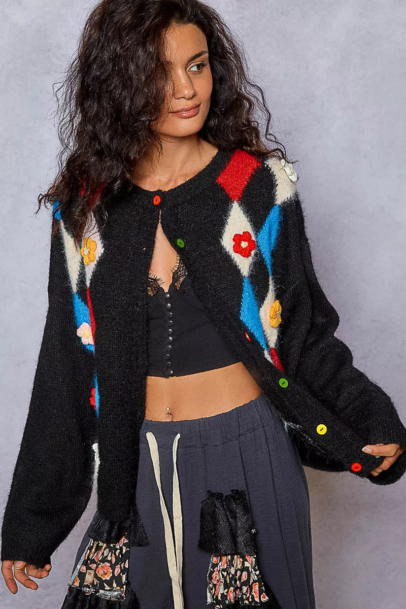 Front view of model wearing black cardigan with colorful argyle pattern and floral accents