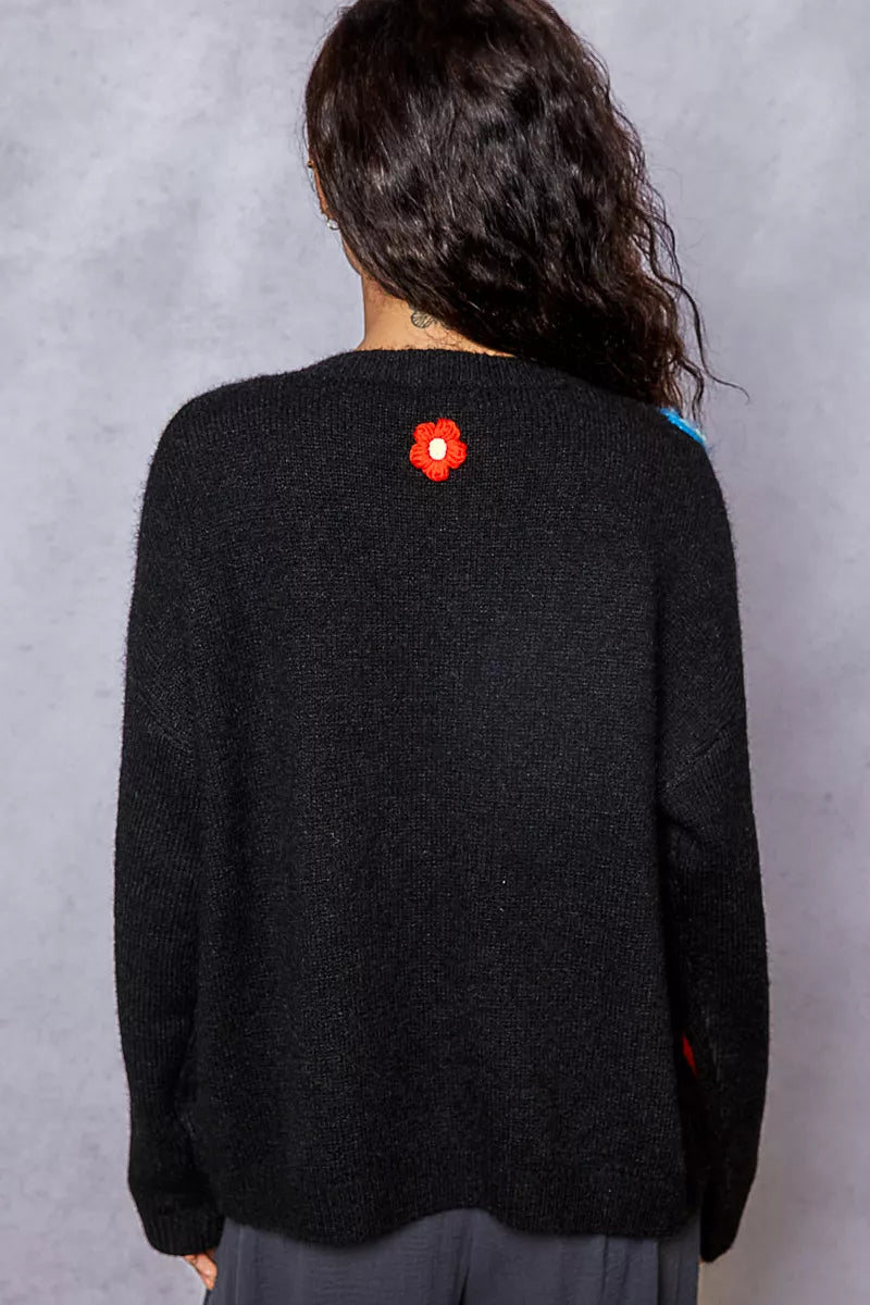 Back view of model wearing black cardigan with colorful argyle pattern and floral accents