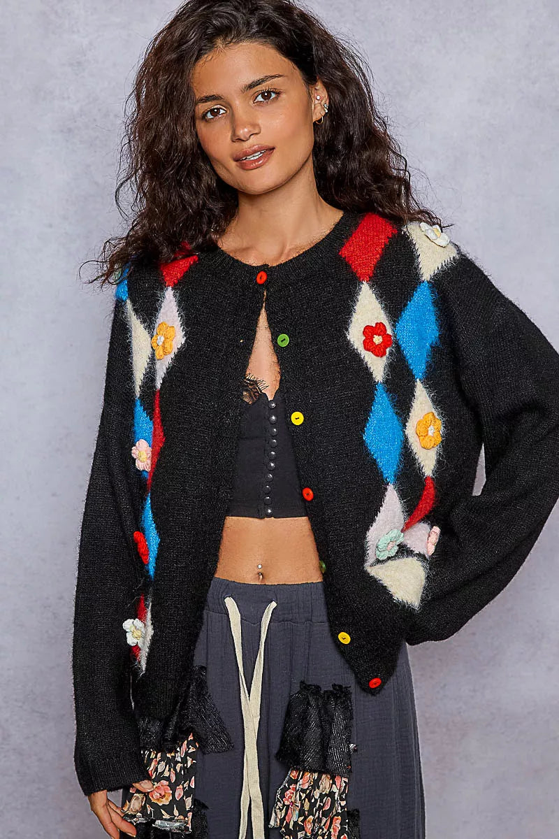 Front view of model wearing black cardigan with colorful argyle pattern and floral accents