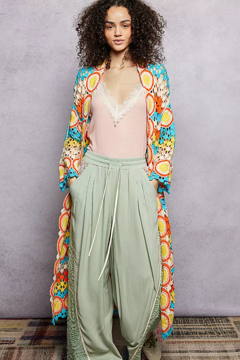 Long colorful openwork crochet duster with circle motifs and scalloped edges, worn over a pastel outfit.
