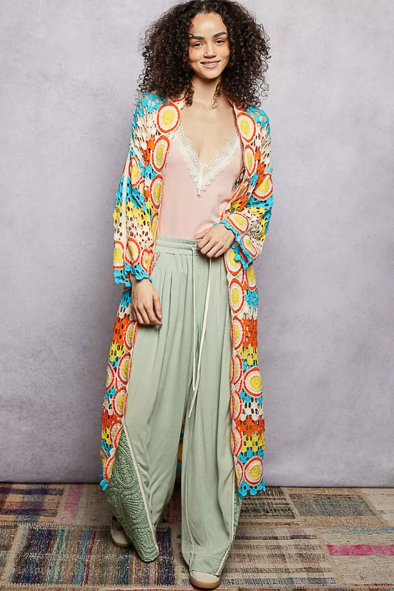 Long colorful openwork crochet duster with circle motifs and scalloped edges, worn over a pastel outfit.