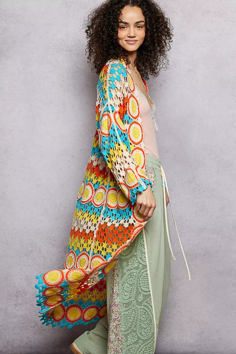Long colorful openwork crochet duster with circle motifs and scalloped edges, worn over a pastel outfit.