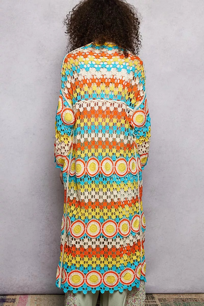 Long colorful openwork crochet duster with circle motifs and scalloped edges, worn over a pastel outfit.