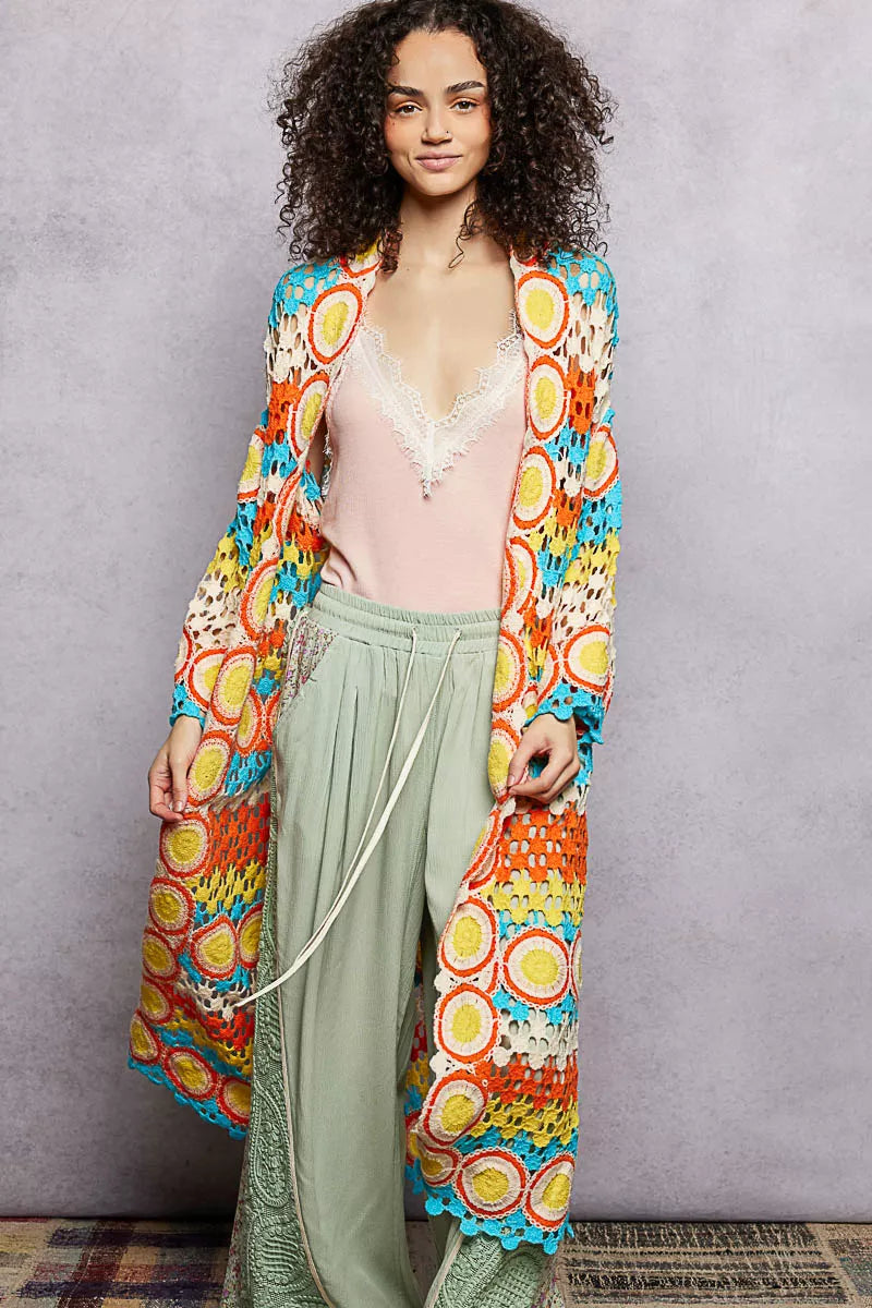 Long colorful openwork crochet duster with circle motifs and scalloped edges, worn over a pastel outfit.