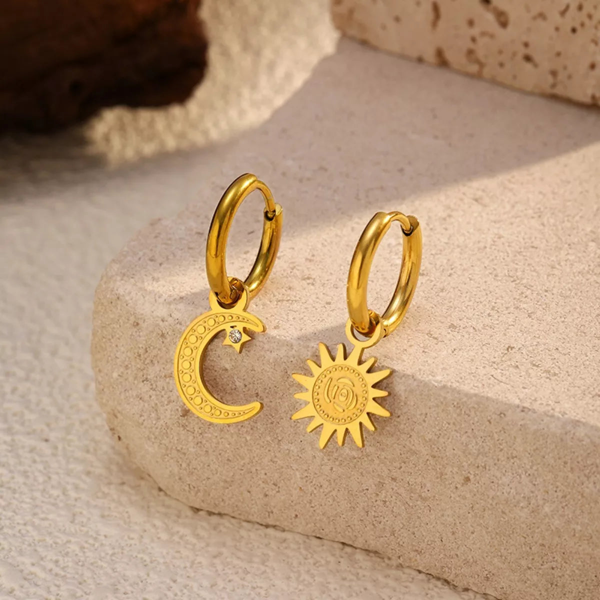 Sun and moon charm hoop earrings with celestial design in gold and silver tones displayed on a neutral stone background