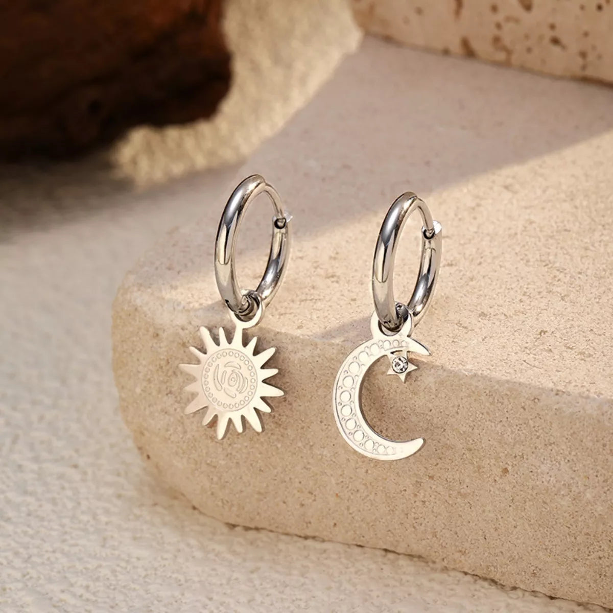 Sun and moon charm hoop earrings with celestial design in gold and silver tones displayed on a neutral stone background