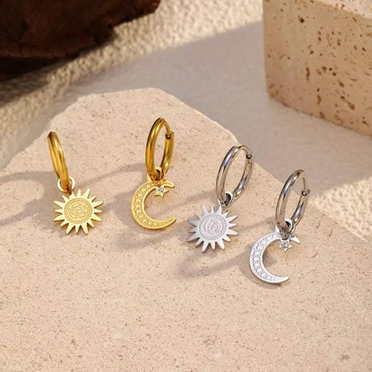 Sun and moon charm hoop earrings with celestial design in gold and silver tones displayed on a neutral stone background