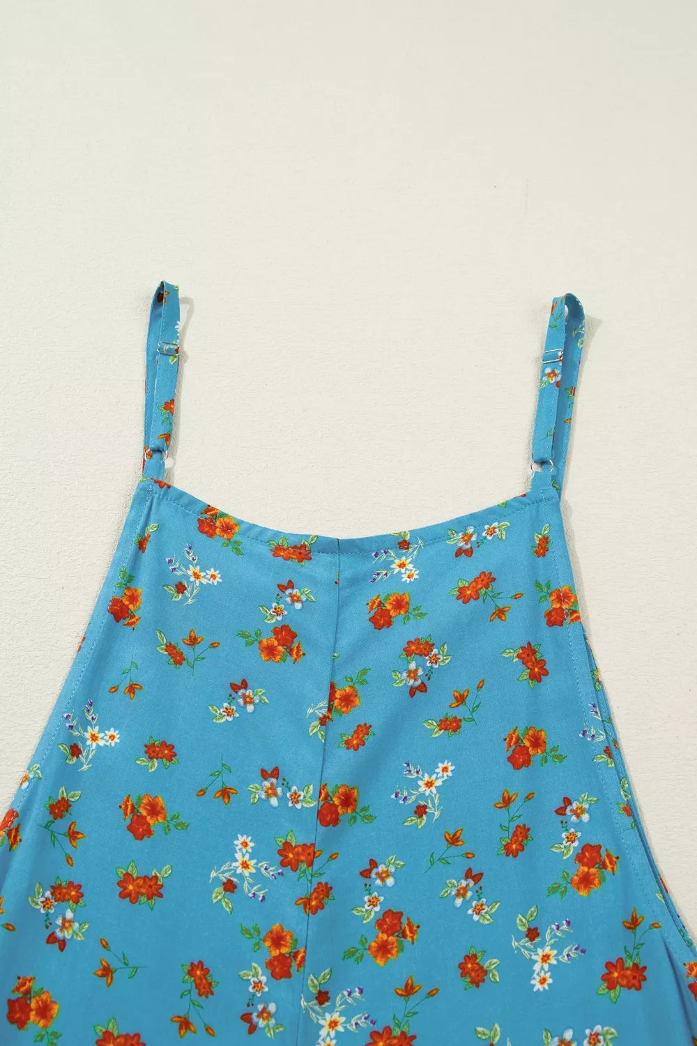 Blue floral wide-leg jumpsuit with thin straps, relaxed flowy fit, and side pockets styled with sandals.