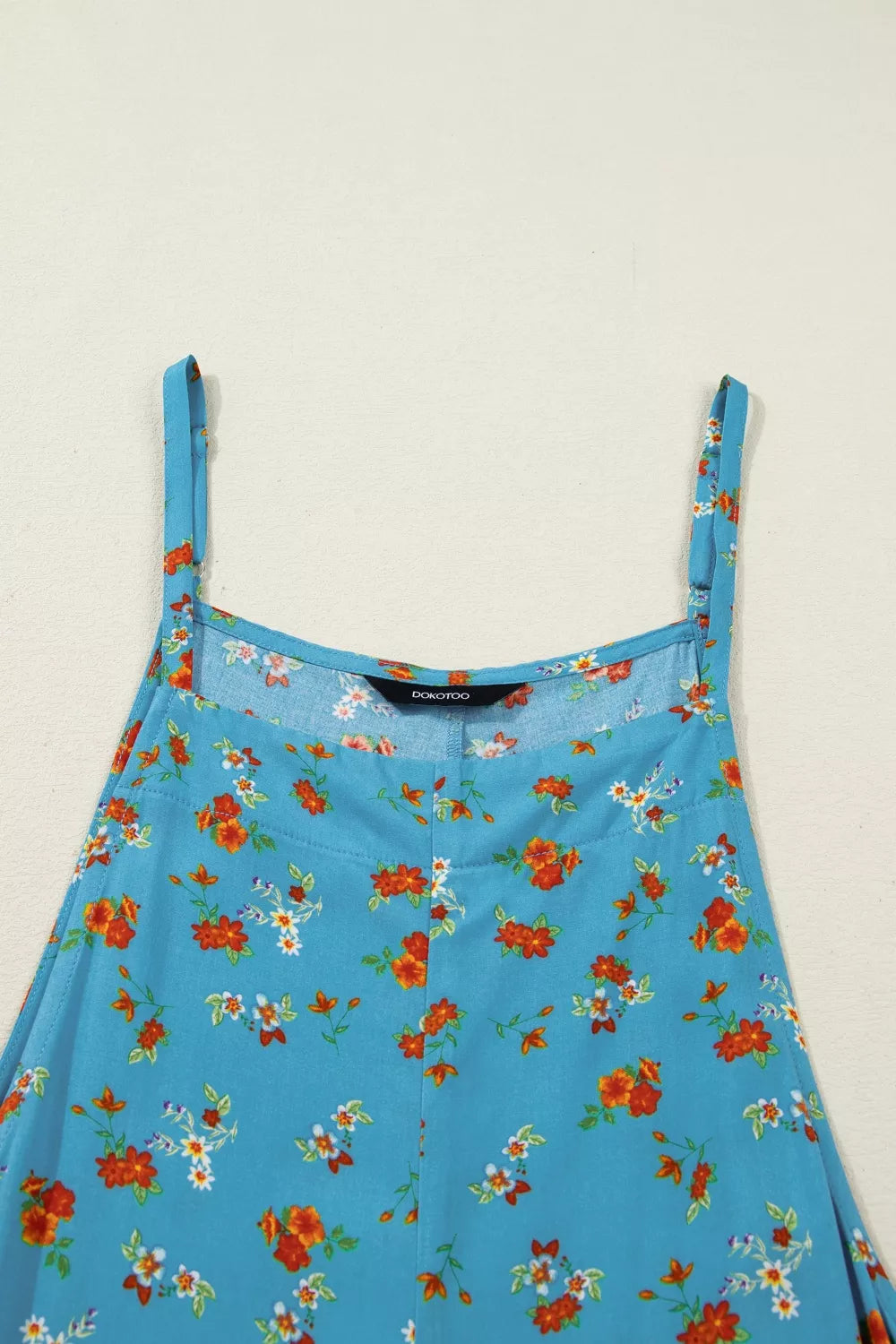 Blue floral wide-leg jumpsuit with thin straps, relaxed flowy fit, and side pockets styled with sandals.