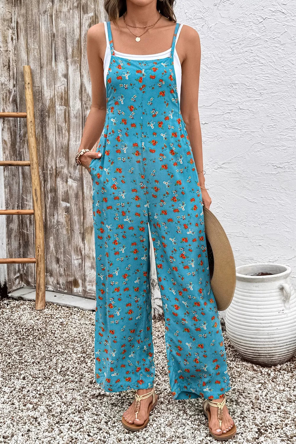 Blue floral wide-leg jumpsuit with thin straps, relaxed flowy fit, and side pockets styled with sandals.