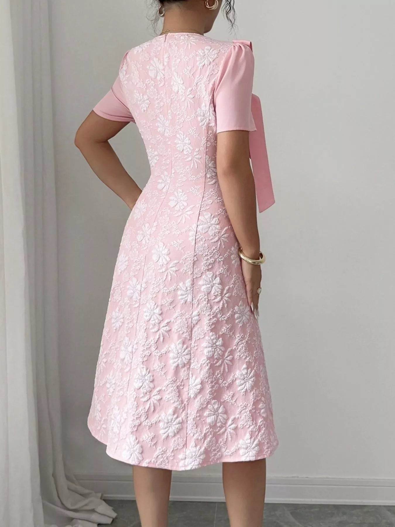 Woman wearing pink Cherry Blossom Charm Midi Dress with white floral embroidery and bow detail at shoulder, elegant midi party dress.