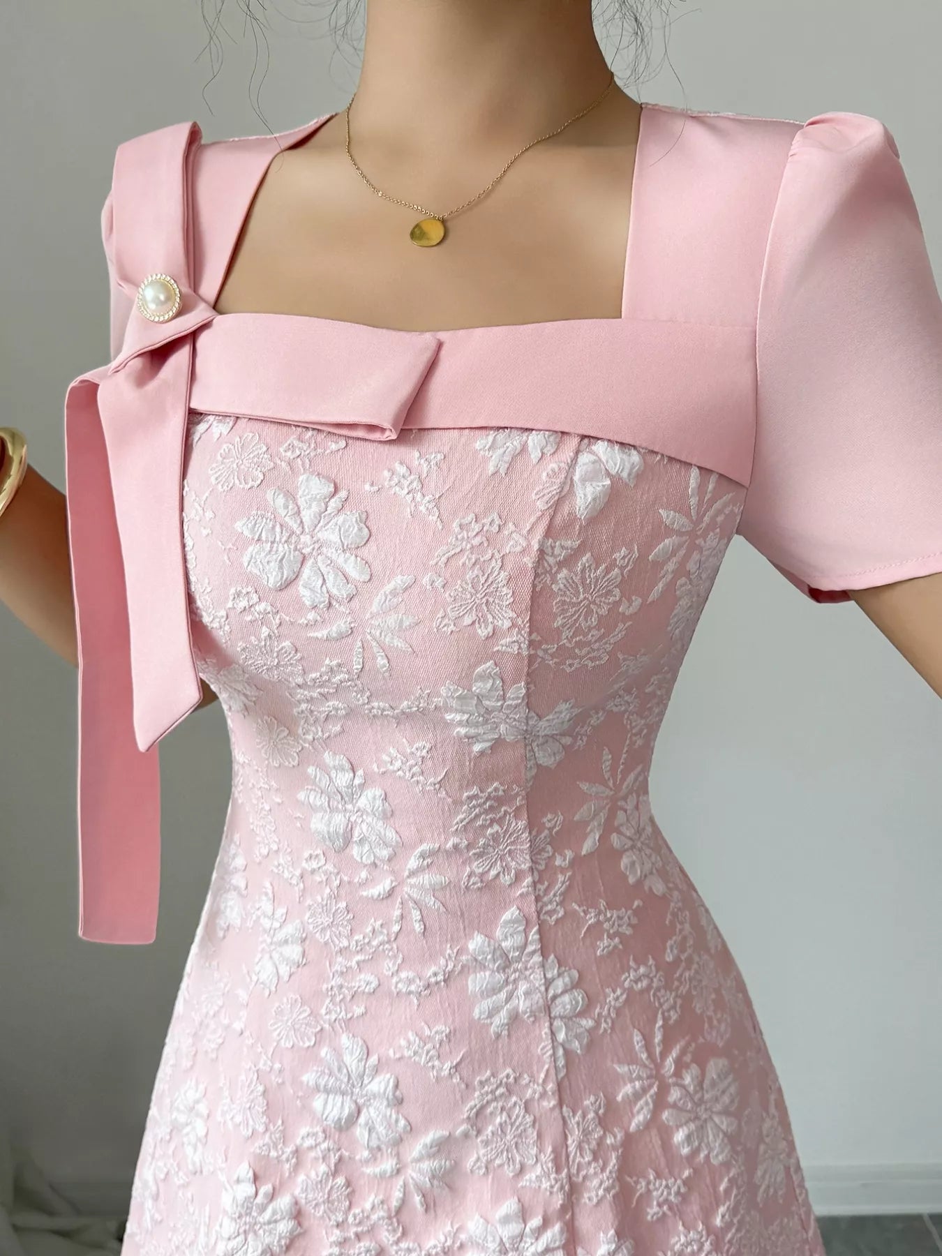 Woman wearing pink Cherry Blossom Charm Midi Dress with white floral embroidery and bow detail at shoulder, elegant midi party dress.