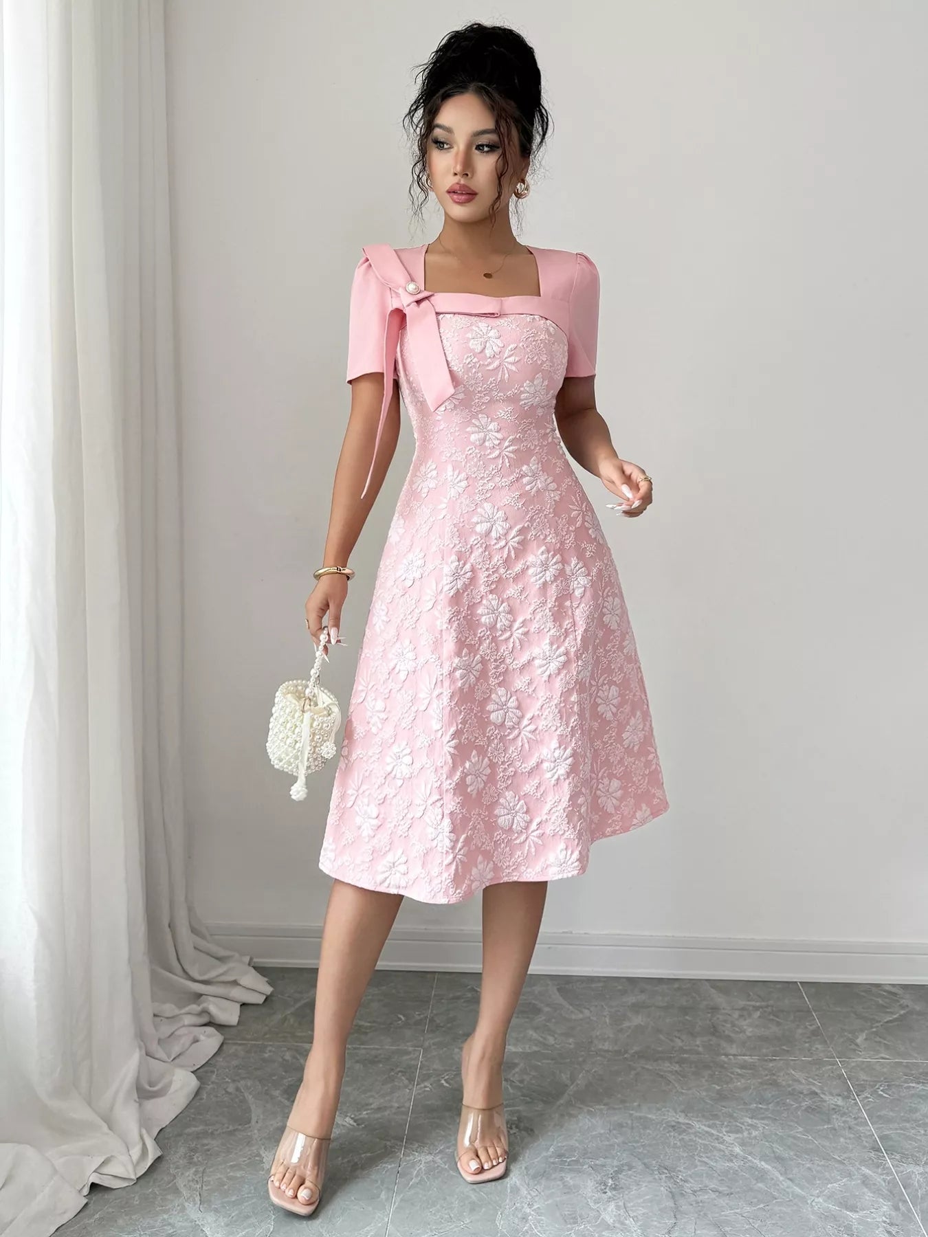Woman wearing pink Cherry Blossom Charm Midi Dress with white floral embroidery and bow detail at shoulder, elegant midi party dress.