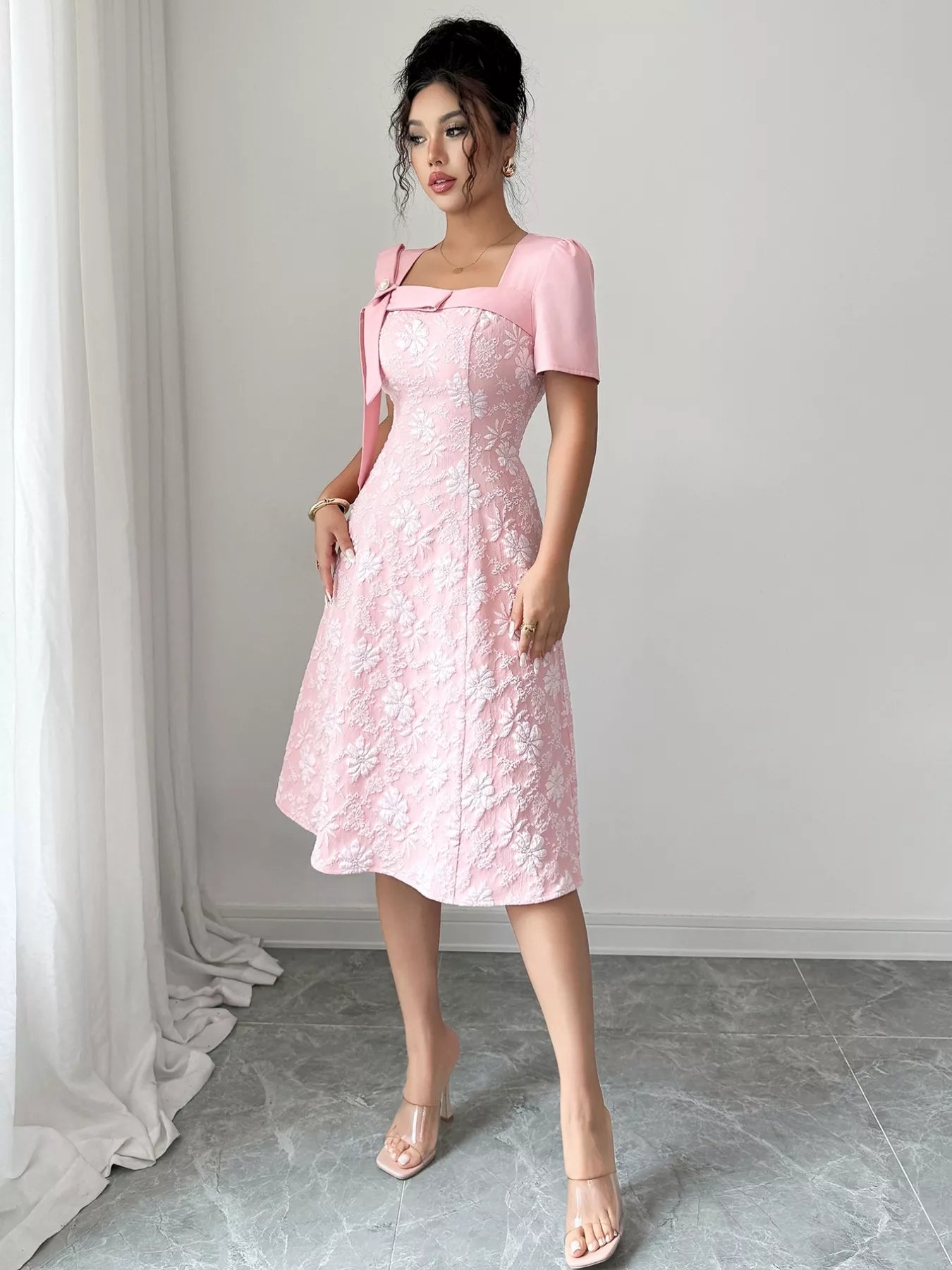 Woman wearing pink Cherry Blossom Charm Midi Dress with white floral embroidery and bow detail at shoulder, elegant midi party dress.