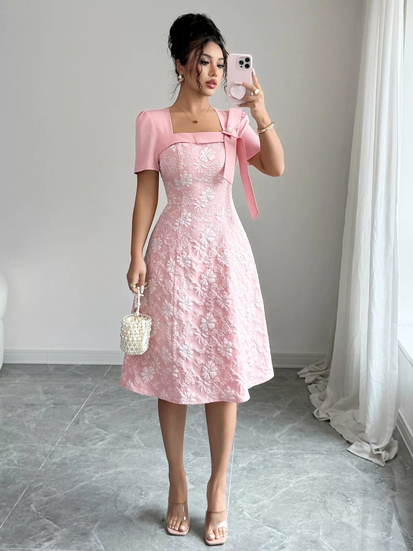 Woman wearing pink Cherry Blossom Charm Midi Dress with white floral embroidery and bow detail at shoulder, elegant midi party dress.